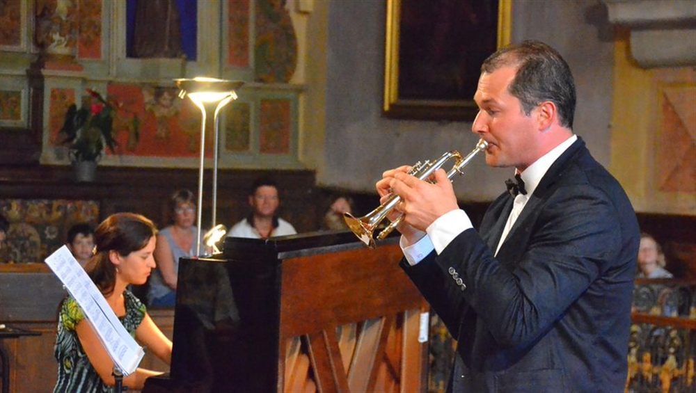 Mélanie Adler en robe bleue et Laurent Jammes avec son instrument en cuivre, devant un autel